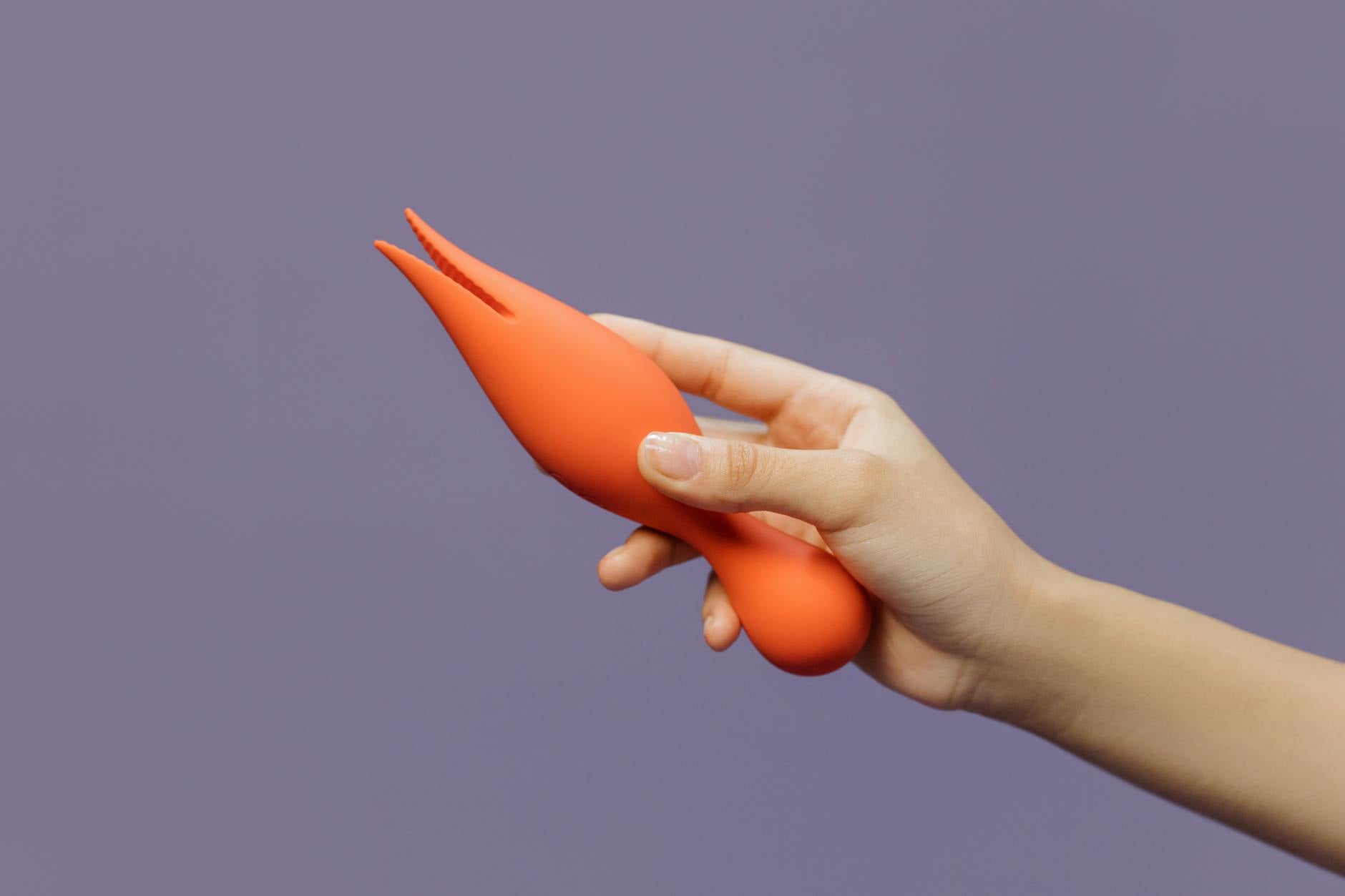 Close-up of a hand holding a lemon clitoral vibrator against a purple backdrop, showcasing modern sensuality