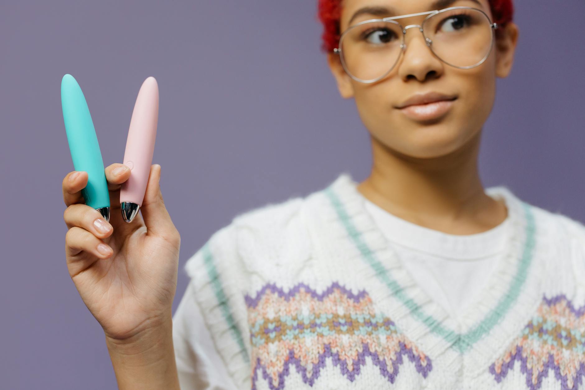 Intimate close-up of hands holding a sleek blue vibrator against a purple background.